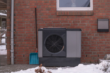 Outdoor air source heat pump unit installed beside brick residential building in winter conditions...