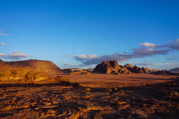 Naklejka premium Wide desert landscape with sandstone rock formations under blue sky. Wadi Rum inspired scenery, minimal and vast wilderness, travel and nature background.