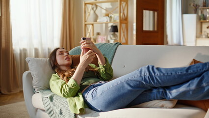 Positive woman video calling by smartphone reclining sofa at home. Lady talking