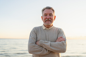 Fototapeta premium Outdoor portrait of confident stylish European middle aged senior man on beach. Older mature man smiling. Happy senior grandfather looking at camera close up face headshot portrait. Happy people