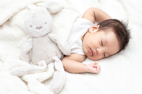 Top view of a baby sleeping on a bed. With a white doll rabbit. Beautiful portrait of a small asian baby. A cute little newborn baby in a blanket.