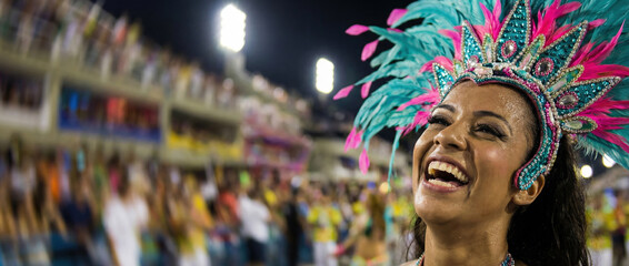 Beautiful smiling samba dancer with colorful feather headdress at the Rio Carnival parade. Happy Brazilian woman celebrating in the Sambadrome at night with blurred crowd background.