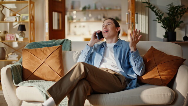 Cheerful guy gossiping cellphone at couch home closeup. Man enjoy friendly call
