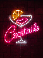 Neon cocktails sign with glowing glass on brick wall