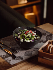 Fresh vegetable salad with cheese in dark ceramic bowl on table