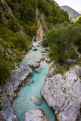 Turquoise Soca Isonzo River flowing through a rocky alpine gorge with clear water, boulders and green forest in Slovenia near Bovec