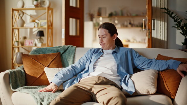 Exhausted brunette sitting couch looking around bored face at home. Tired man