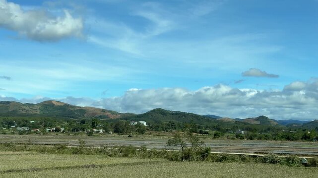 Rows of green farmland and distant rises pass steadily, slow motion emphasizing scale, distance, and everyday rural life beyond cities. Agrarian travel.