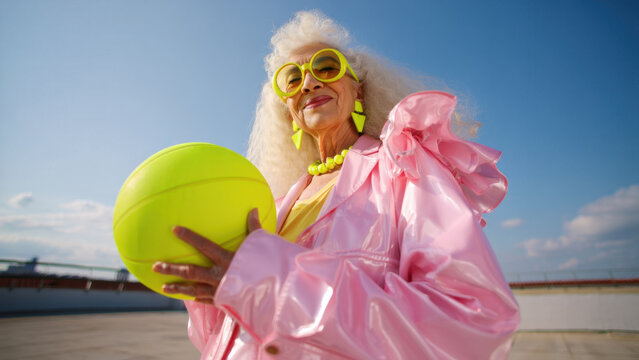 Vibrant senior fashion on a sunlit rooftop featuring neon yellow accessories and a pink metallic coat, bold chunky jewelry, retro glamour, expressive confidence, urban portrait moment today - Powered by Adobe