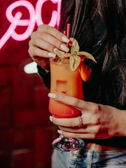 Woman holding layered cocktail with neon lights and brick wall background