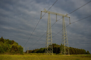 High voltage electricity transmission lines running through forest and open field, energy...