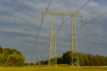 High voltage electricity transmission lines running through forest and open field, energy infrastructure in natural landscape. Power distribution, grid connection and industrial energy concept.
