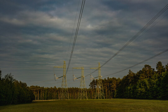 High voltage electricity transmission lines running through forest and open field, energy infrastructure in natural landscape. Power distribution, grid connection and industrial energy concept.
