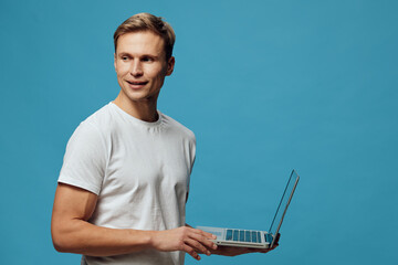 smiling young man holding laptop wearing white t-shirt looking side standing on blue background freelancer digital nomad remote work concept