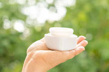 hand holds jar smooth, natural-looking cream, symbolizing gentle skincare and holistic beauty routines, skincare product presented in nature&rsquo;s light, emphasizing purity and organic ingredients