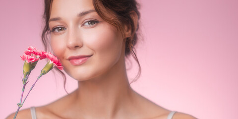 Radiant Woman Holding Carnations and Smiling in Soft Pink Light