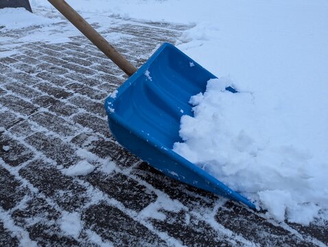 Vivid blue plastic shovel against white snow on pavement, minimal winter scene illustrating snow shoveling, seasonal chores, and cold outdoor conditions.