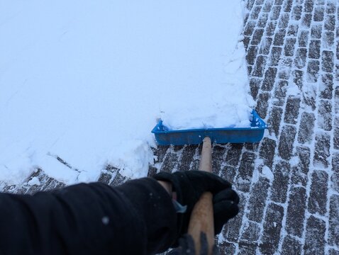 Single blue snow shovel on snowy sidewalk, clean composition emphasizing winter weather, cold air, and the everyday effort of clearing paths and driveways after snowfall.