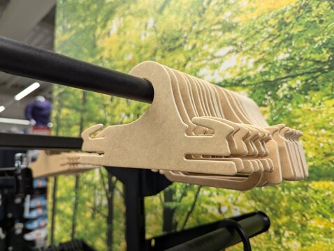 Natural cardboard hangers arranged on a metal clothing rack inside a store, green foliage background image creating a clean, eco-friendly mood for fashion retail and organization themes.