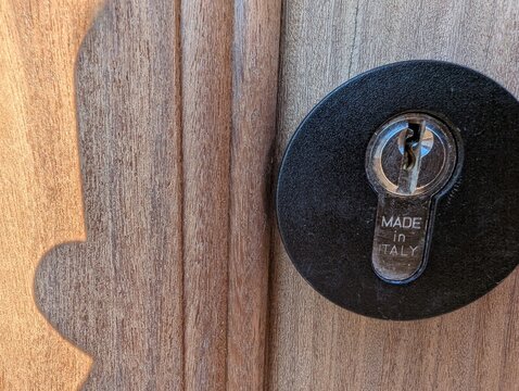 Close-up of a modern door lock on textured wooden door with visible wear from impact, circular black escutcheon and Made in Italy label, ideal for home security, hardware, and design themes.