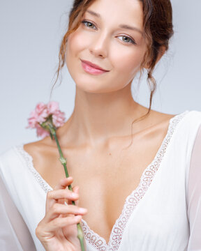 Graceful Young Woman With Pink Flower And Soft Smile In White Dress
