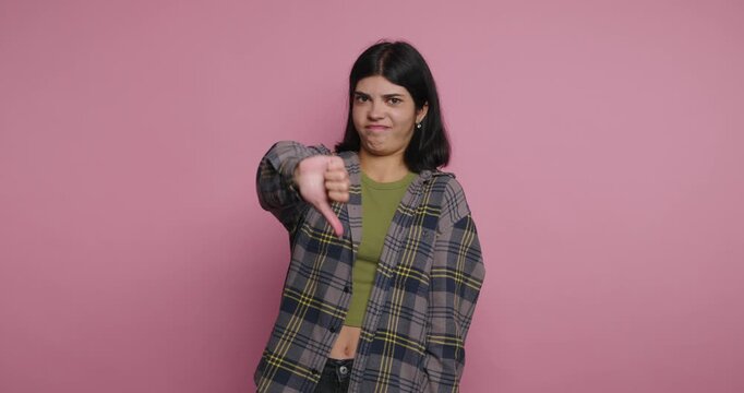 Young woman stands against pink background and shows a range of emotions during a personal expression exercise. girl shows a dislike gesture