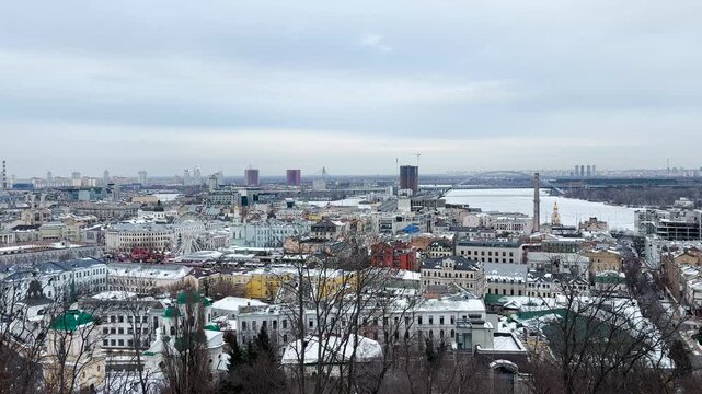 A panoramic view of snowy Podil unfolds from Volodymyrska Hill, revealing a calm winter cityscape in Kyiv, Ukraine.