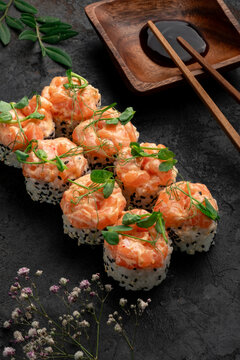 Premium salmon sushi rolls topped with creamy salmon tartare and microgreens, served with soy sauce and chopsticks on a dark elegant background. Luxury Japanese maki, gourmet seafood fusion