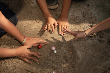 Children playing marbles in the schoolyard during recess. Traditional game, shared section of group play. Socializing. Inclusion. Fine motor skills