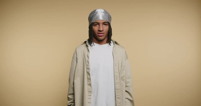 Young man waves hello indoors showing a bright smile in a simple setting with plain background and relaxed vibe in daytime