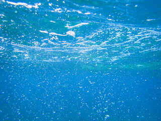 Obraz premium Underwater photography of the deep ocean with the ocean surface rippled with bokeh, bubbles, and lens flare great for water background with room for copy, Sunlight underwater with air bubbles rising.