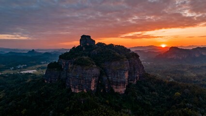 Fototapeta premium Aerial view of a rocky mountain peak at sunset with vibrant orange and pink sky over a forested landscape