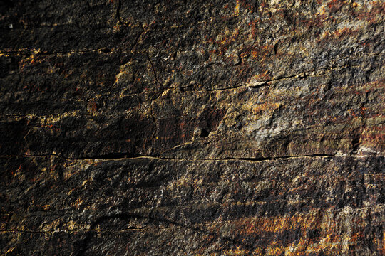 Primer plano de roca metam&oacute;rfica con foliaci&oacute;n en capas, bandas minerales y tonos oxidados en gris y naranja.presi&oacute;n geol&oacute;gica y transformaci&oacute;n, simbolizando resistencia, historia natural ,complejidad