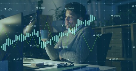 Holding man in knit sweater lifting mug to mouth at home office, with monitor and charts