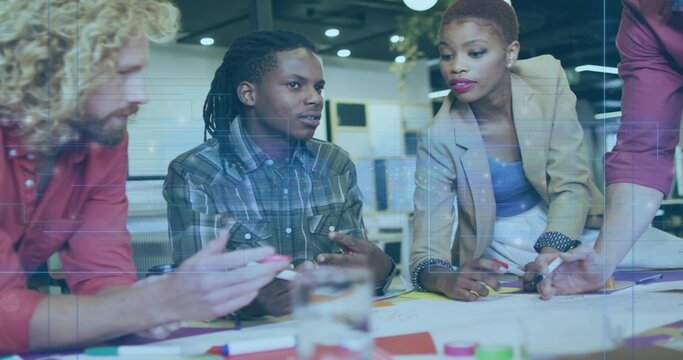 Discussing four coworkers in business attire reviewing papers, color cards and pens in open office - Powered by Adobe