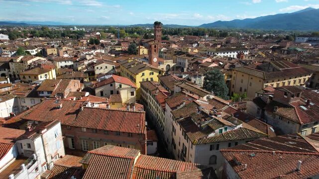 Aerial 4K view of Lucca skyline, flying from the historic Clock Tower (Torre delle Ore) towards Guinigi Tower with oak trees, Tuscany, Italy.