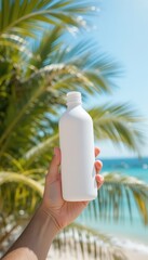 Human hand holding a blank white bottle Tropical beach setting with green palm fronds clear blue sky and turquoise ocean