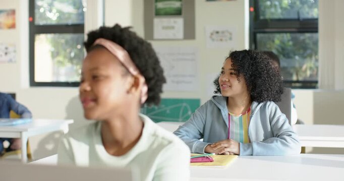 African American teen girls turning toward teacher after prompt in classroom smiling with notebook
