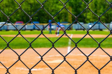 Selective focus on a chain link fence at a youth baseball game blurred in the background.