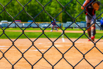 Selective focus on a chain link fence at a youth baseball game blurred in the background.