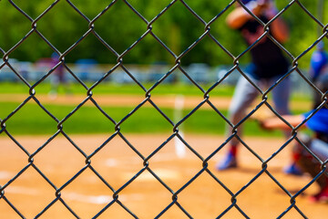 Selective focus on a chain link fence at a youth baseball game blurred in the background.