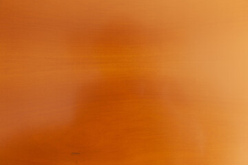 Superficie de madera pulida con veta sutil y tono cálido.Primer plano de superficie de madera lisa color naranja-marrón con veta horizontal, sombra tenue y marca oscura. © C.Castilla