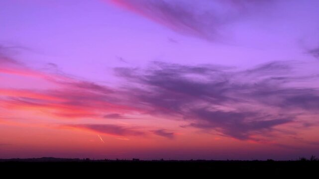Fantasy colored sunset sky sun and gentle colorful clouds over a field fast time lapse horizon. Bright color skyscraper sun and cirrus clouds and meadow, timelapse landscape beautiful background 4K.