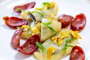 Gourmet Ukrainian pierogi, filled with black beans and served with fried garlic and grilled sausage, garnished with sliced ​​fresh scallions.