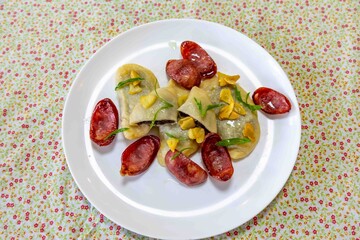 Gourmet Ukrainian pierogi, filled with black beans and served with fried garlic and grilled sausage, garnished with sliced ​​fresh scallions.