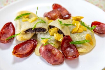 Gourmet Ukrainian pierogi, filled with black beans and served with fried garlic and grilled sausage, garnished with sliced ​​fresh scallions.