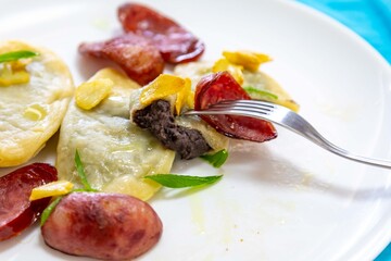 Gourmet Ukrainian pierogi, filled with black beans and served with fried garlic and grilled sausage, garnished with sliced ​​fresh scallions.