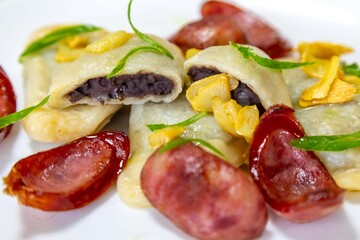 Gourmet Ukrainian pierogi, filled with black beans and served with fried garlic and grilled sausage, garnished with sliced ​​fresh scallions.