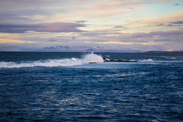 Obraz premium Waves Breaking on Rocky Reef with Distant Mountains and Dramatic Sky, Iceland
