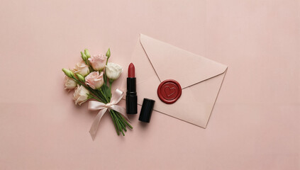 Romantic flat lay with roses, red lipstick and sealed letter on a pastel pink background